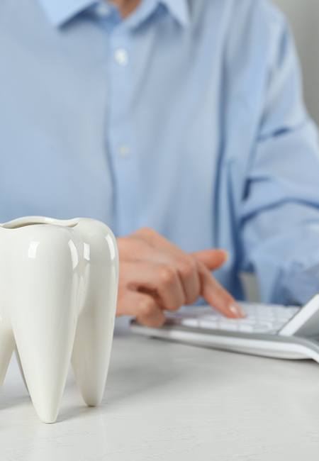 A patient using a calculator next to a large model tooth and stacks of silver coins