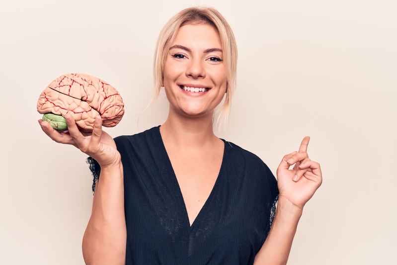 A smiling woman holding a model brain while pointing with her finger